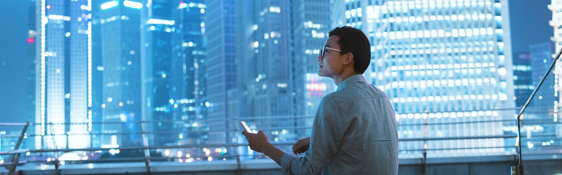 Jeune homme regardant son smartphone sur le toit d'un immeuble en ville la nuit