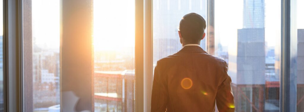 Geschäftsmann schaut durch Bürofenster im Sonnenlicht