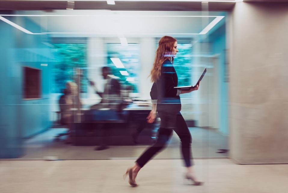 사무실에서 노트북 컴퓨터를 들고 빠르게 걸어가는 여성