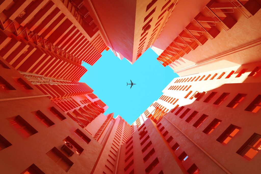 오렌지 빌딩 사이로 하트 모양의 푸른 하늘 위에 비행기가 날아가는 디지털 생성 이미지