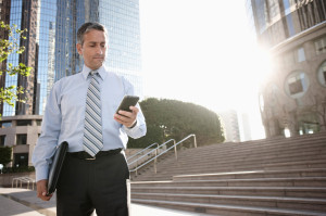 Hispanic businessman text messaging on cell phone outdoors