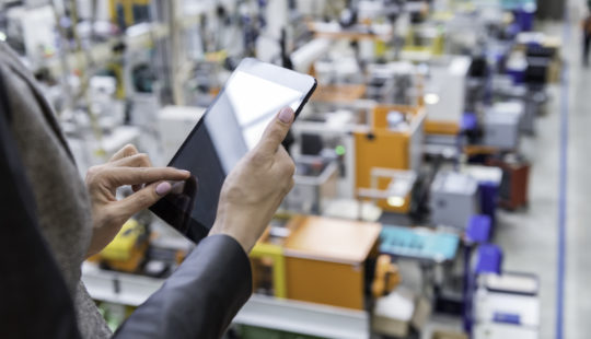 Female manager holding black tablet, futuristic machines in background in factory