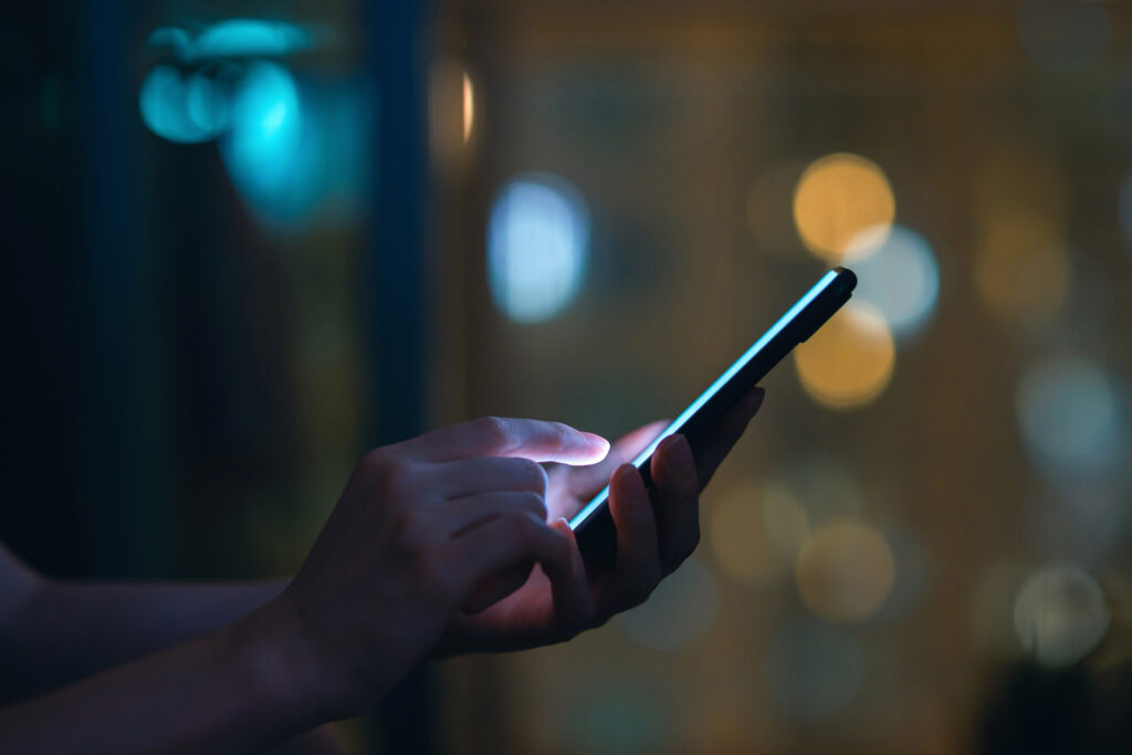 Close up of hand using smartphone in the dark, against illuminated city light