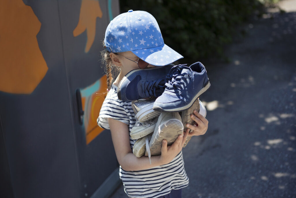 Child carrying pile of old shoes for recycling at a recycling center