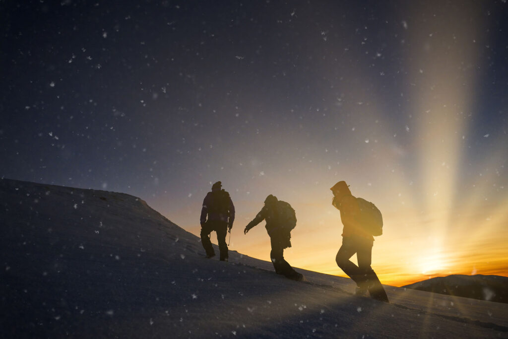 Three hikers climbing up mountain during sunset