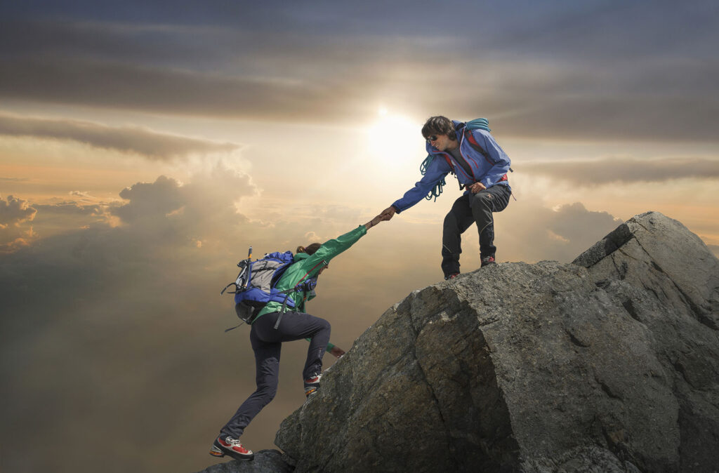 Climber helping partner reach mountain top