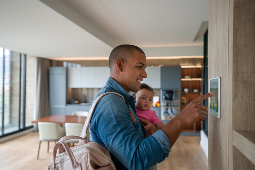 Happy Latin American man leaving the house with his baby and locking the door using a home automation system and smart home concepts