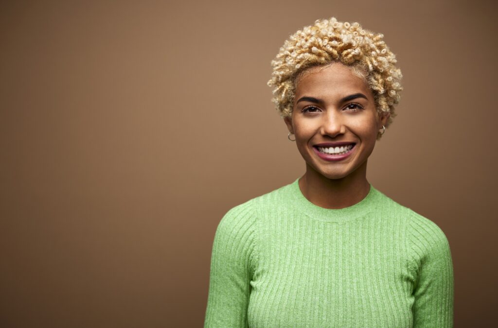 Portrait of young businesswoman smiling. Close-up of confident female professional is having short blond hair. She is wearing green top against brown background