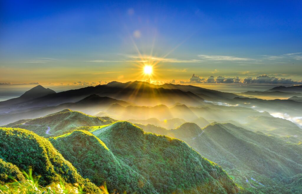 View of sun rise with mountain against blue sky.