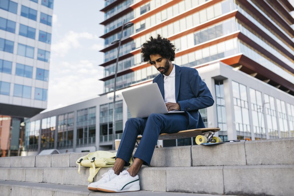 Spain, Barcelona, young businessman sitting outdoors in the city working on laptop