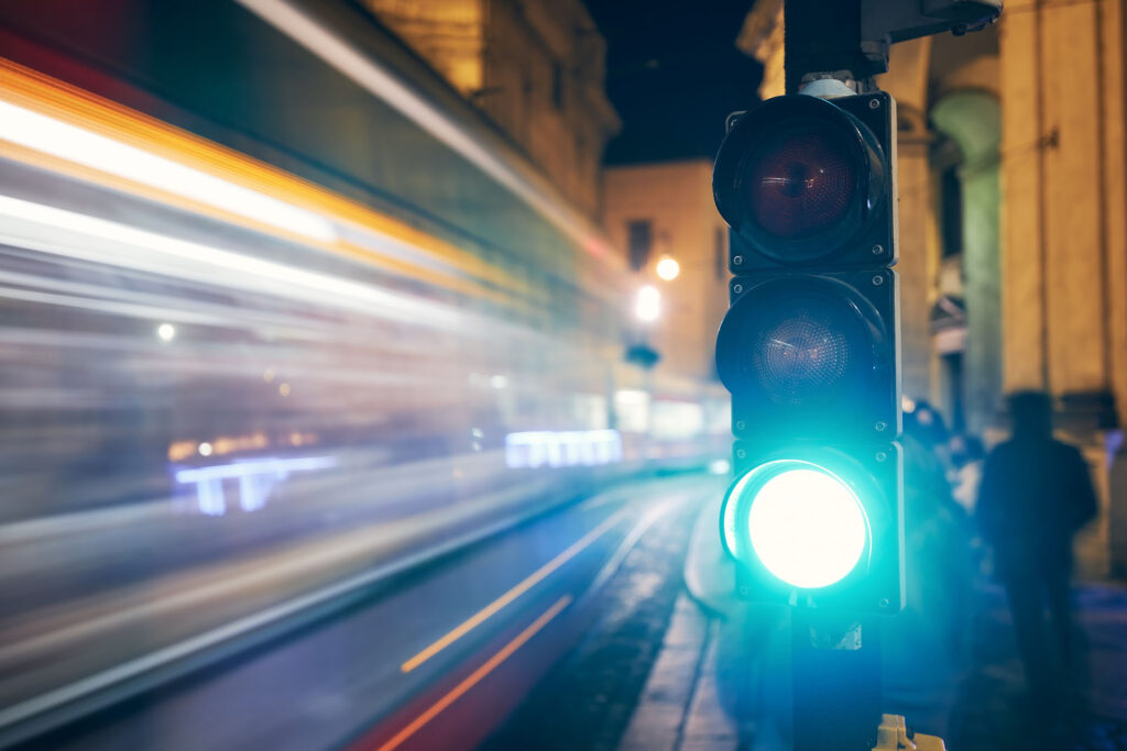 Green On Traffic Light Against Light Trails Of Tram And Cars. Night Scene Of City Street