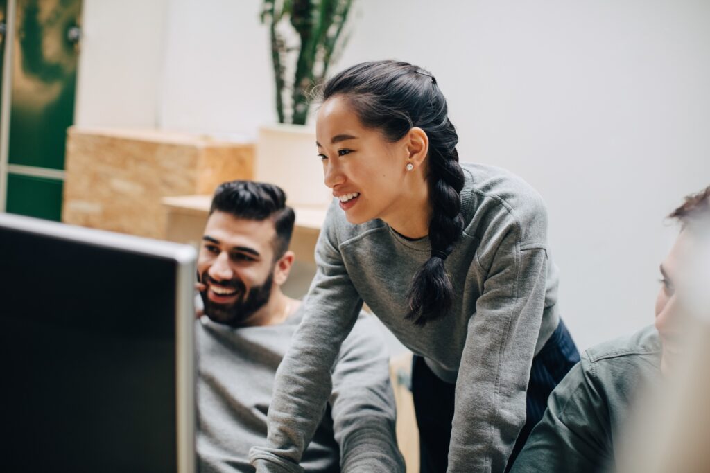 Smiling coworkers looking at computer while working in office