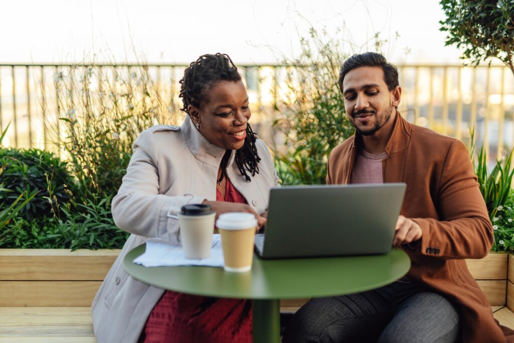 Coworkers discussing project and having work meeting at rooftop garden in high-rise office building. Multiracial business team working outdoor. They're having coffee.