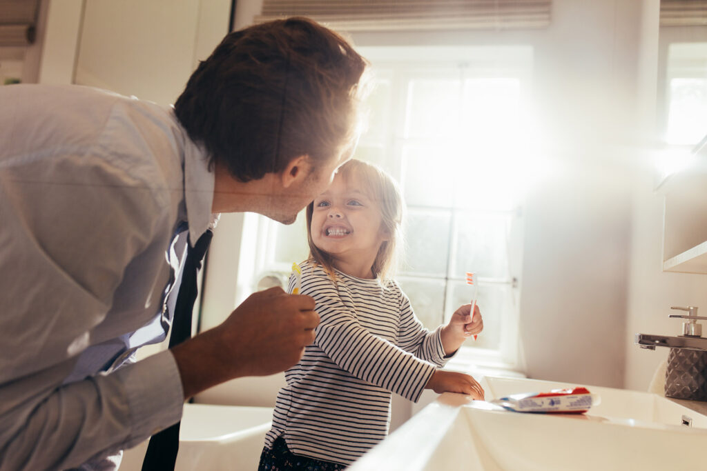 Father and daughter brushing teeth standing in bathroom and looking at each other