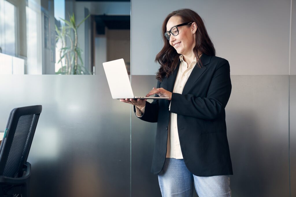 A woman at a computer in a modern office. Working from the office, a business woman in eyeglasses is typing a message on a laptop. Copy Space