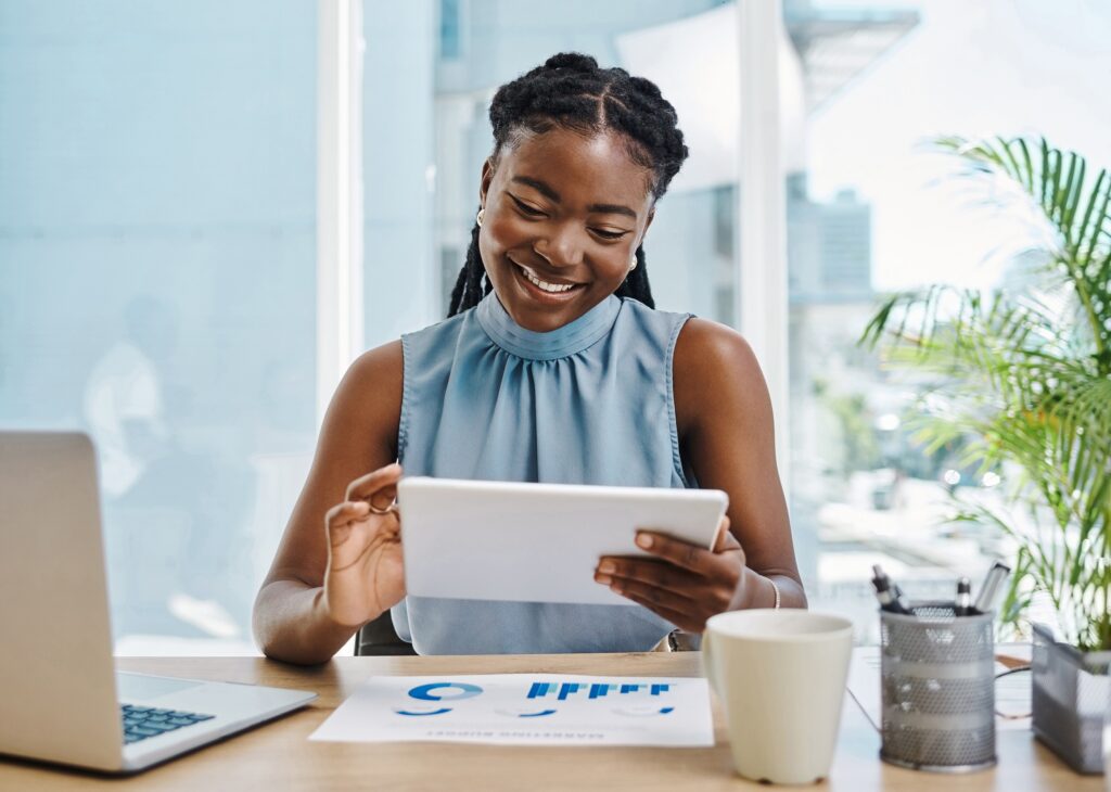 Confident young african businesswoman using a digital tablet while reviewing graphs and data in an office alone