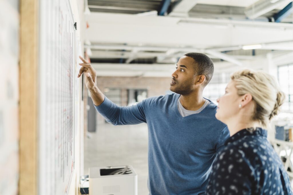 A photo of businessman discussing with female colleague over whiteboard. Professionals are analysing new strategy. They are in creative office.