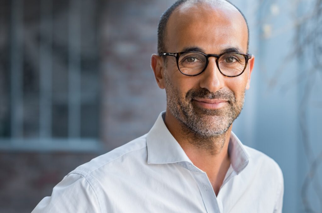 Portrait of happy mature man wearing spectacles and looking at camera outdoor. Man with beard and glasses feeling confident. Close up face of hispanic business man smiling.